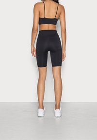 Černá sportovní podprsenka bez švů s tenkými ramínky, doplněná o černé cyklistické šortky s vysokým pasem a bílé sportovní boty.
