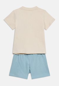 Μπεζ κοντομάνικη μπλούζα συνδυασμένη με ανοιχτό μπλε σορτς με ελαστική μέση, απλωμένα επίπεδα, δείχνοντας την πίσω πλευρά και των δύο ρούχων.