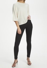 Weißes geripptes Stricktop mit Batik-Ausschnitt und kurzen Ärmeln, kombiniert mit schwarzen, engen Jeans und schwarzen, verstellbaren hochhackigen Sandalen.