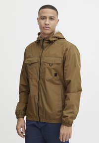 Brown lightweight jacket with a hood, featuring two chest pockets, black zipper, and elastic cuffs. Smooth texture, casual design.