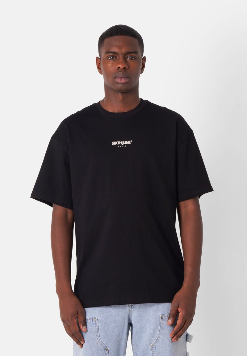 Camiseta de algodón negra de manga corta, con cuello redondo y logotipo impreso "SIXTHJUNE" en el pecho, combinada con jeans azules claros.