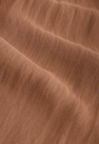 Gros plan sur un tissu doux côtelé de couleur marron chaud, montrant de fines lignes verticales et de douces pliures créant des ondulations texturées.