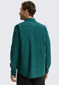 Grøn skjorte med lange ærmer, klassisk krave og glat tekstur, med en lige kant og knaplukning ved ærmerne.