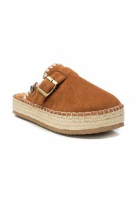 Zueco marrón de ante sin cordones con suela de yute trenzado, que presenta una hebilla dorada y costuras blancas a lo largo del borde. Diseño de punta redondeada y plana.