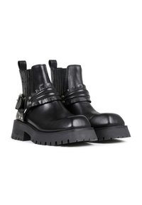 Botas de cuero negro hasta el tobillo con paneles de tela acanalada, suela de goma gruesa, acentos metálicos y correas envueltas para un detalle adicional.