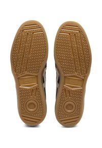 Brown rubber shoe soles with a textured wave pattern, circular emblem, featuring a light beige edge for grip and support.