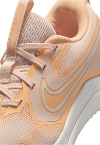 Zapatilla Nike Cosmic Runner con parte superior de malla en color durazno claro, detalles texturizados y suela blanca. Incluye el logo Nike swoosh en color plata.