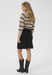 Beige striped sweater, mustat hameet ja mustat cowboy-kengät. Neulepaita on muotoiltu tiiviisti; hame on polvipituinen ja hieman levenevä.