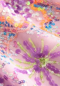 Tissu à paillettes en filet rose, orné de paillettes multicolores en violet, orange et bleu, disposées en un motif floral avec des textures variées.
