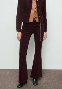 Pantaloni a palazzo in corduroy bordeaux abbinati a un top marrone, con dettagli a catena in vita e stivaletti neri alla caviglia. Tessuto morbido.