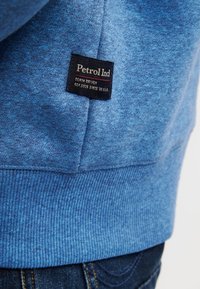 Felpa blu con finitura testurizzata, caratterizzata da un'etichetta nera con la scritta "Petrol Ind" cucita sull'orlo. Il tessuto ha un aspetto morbido e informale.