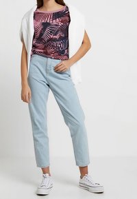 Różowa bluzka z krótkim rękawem w ciemny wzór liści, zestawiona z jasnoniebieskimi dżinsami i białymi trampkami. Biała kardigan narzucony na ramiona.