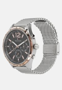 Montre avec un bracelet en maille argentée de Tommy Hilfiger, dotée d'un cadran noir, d'accents en or rose, de grands chiffres et de trois sous-cadrans pour la date et l'heure.