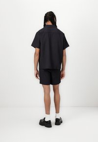Sort kortærmet skjorte og shorts sæt med lodrette striber, lavet af et tekstureret stof. Har en løs pasform og subtile folddetaljer.