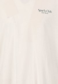 T-shirt en coton blanc avec un décolleté en V et un petit logo vert foncé sur le côté supérieur gauche portant l'inscription "Sports Club Les'Arcs".
