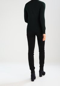 Czarne, dopasowane dżinsy o gładkiej fakturze, w połączeniu z ciemnozieloną bluzką z długim rękawem. Całość uzupełniają wyróżniające się botki na wysokim obcasie.