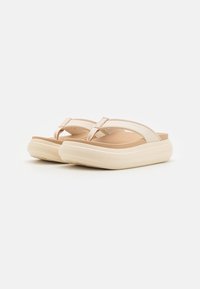 Light beige flip-flop sandals with a soft textured footbed, thick white sole, and minimalist strap design. No visible patterns or logos.