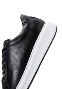 Sneaker in pelle nera con una texture liscia, suola in gomma bianca e lacci neri. Caratteristiche: punta rotonda e dettagli di cucitura minimi.