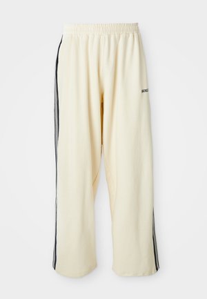 Gai bēšas platās bikses, kas izgatavotas no mīkstas auduma ar elastīgu jostu, ar melnām sānu svītrām un mazu logo detaļu.