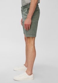 Shorts khaki en coton, avec une coupe slim, des poches latérales et un bouton décoratif au dos. Associés à des baskets blanches à lacets.