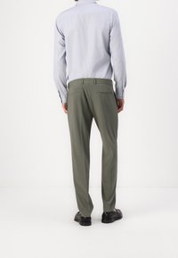 Kakifärgade byxor med rak passform, med två bakfickor och en slät textur. Kombineras med en ljusblå skjorta med knäppning.