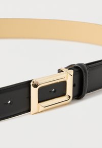 Cintura in pelle nera con fibbia quadrata dorata lucida su uno sfondo neutro.