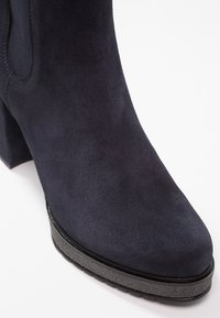 Bottines en daim bleu marine avec un talon bloc et une semelle texturée noire sur fond blanc.