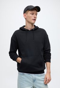 Crna majica s kapuljačom od pamučne mješavine, s džepom na prednjem dijelu, vrpcama za zatezanje i rebrastim manšetama, uparena sa svijetloplavim trapericama.