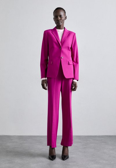 Fuksia värvi kohandatud ülikond, millel on ühe nööbiga bleiser ja laiad püksid, mida täiendab helesinine kõrge kaelusega kampsun ja mustad teravatoalised kontsad.