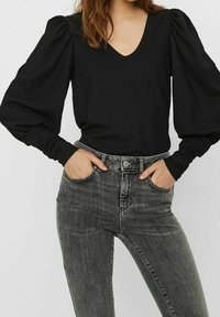 Black v-neck top with voluminous puff sleeves, paired with dark gray high-waisted jeans featuring a subtle fade, stitched accents on pockets.