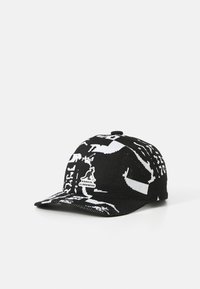 Gorra de punto en blanco y negro con ala curva, que presenta un estampado gráfico y una etiqueta de logo en la parte frontal. Tejido texturizado con un diseño deportivo.