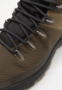 Zapato de senderismo marrón y negro con tejido texturizado, ojales metálicos, cordones duraderos y una suela de goma resistente para tracción.