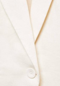 Blazer de color blanco roto con un acabado texturizado, con solapa de muesca y cierre de botón redondo.