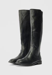 Fekete bőr, térd fölé érő csizma sima felülettel, oldalsó cipzárral, lekerekített orral és alacsony, masszív sarkával.