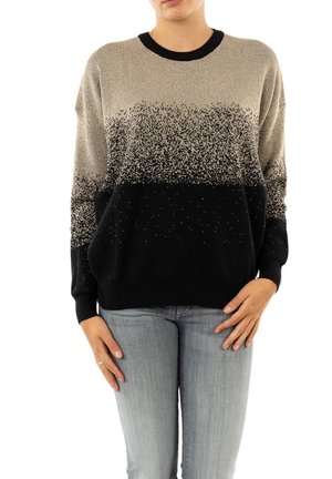 Personne portant un pull à manches longues avec un dégradé tacheté du beige au noir et un jean gris clair, debout avec les mains détendues le long du corps.
