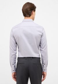 Lichtpaarse langemouwen shirt met knoopschoenen, gladde textuur en getailleerde pasvorm, gecombineerd met donkergrijze broeken met achterzakken.