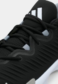 Melns sporta apavu modelis ar reljefu sietveida virsmu, baltām detaļām, pastiprinātu purngalu, melnām kurpju šņorēm un cieši pieguļošu dizainu.