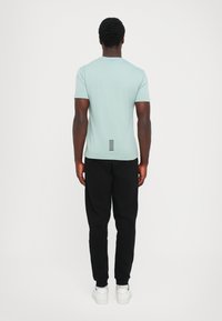 Mintgrønn t-skjorte med korte ermer og rund hals, med vertikal stripe detalj bak, kombinert med svarte joggebukser og hvite sneakers.