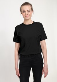Czarna bawełniana koszulka z krótkim rękawem i okrągłym dekoltem, prezentowana na osobie w czarnych dżinsach, charakteryzująca się gładką teksturą.
