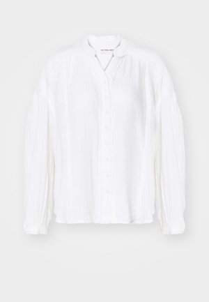 Chemise blanche à manches longues, boutonnée, avec une texture plissée et un col mandarin, offrant une coupe décontractée et des détails de couture subtils.