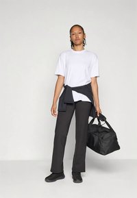 Camiseta blanca de algodón, sudadera negra atada a la cintura, pantalones negros y zapatillas negras. Lleva un bolso de viaje negro con dos asas.