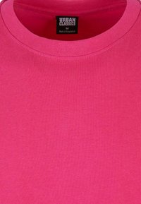 Fukszia színű, pamutból készült kerek nyakú póló, sima textúrával, és egy címkével, amelyen a "URBAN CLASSICS, M, Bangladesben készült" felirat szerepel.