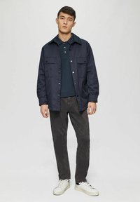 Navy blue button-up jacket with two front pockets, paired with a dark polo shirt and grey pants, and white sneakers. Simple, casual design.