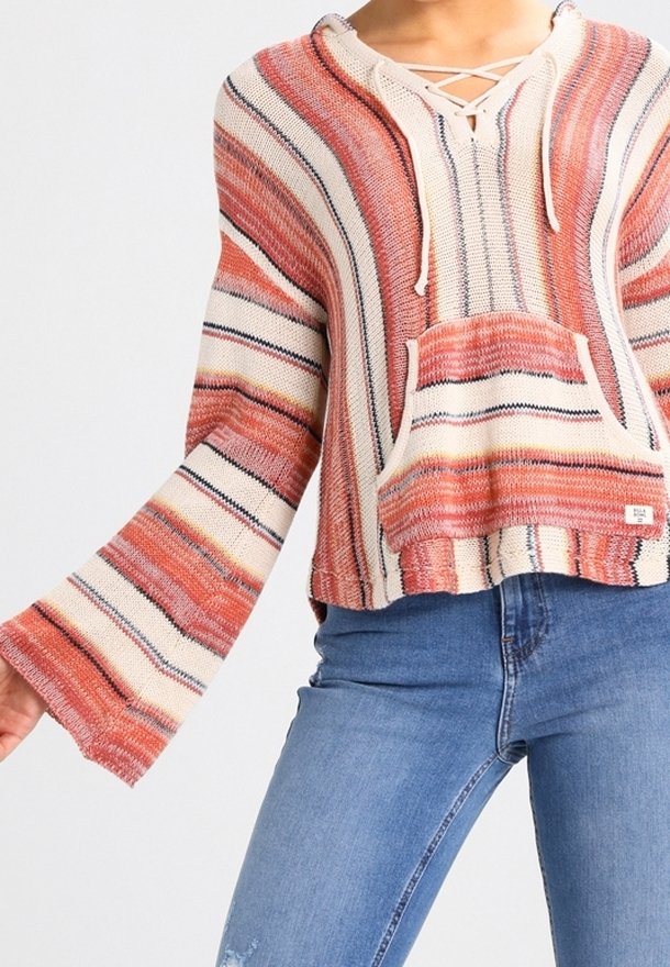Sweat à capuche en maille rayée avec de larges manches cloches dans des tons corail, crème et marine, porté avec un jean bleu sur une personne.