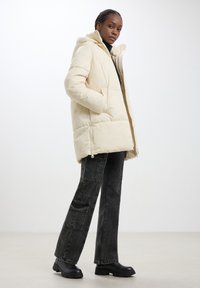 Giacca a vento color crema, dotata di cappuccio, texture trapuntata e zip frontale. Abbinata a pantaloni cargo wide-leg grigio scuro e stivali chunky neri.