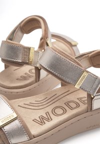 Twee wig sandalen met metallic zilveren banden en tan accenten. Zachte suede binnenzolen met het reliëf "WODEN" logo. Chunky zool ontwerp.