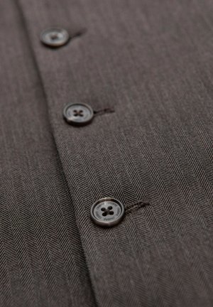 Detalle de un tejido de espiga marrón con tres botones oscuros cosidos en una línea vertical, mostrando la textura y la costura en detalle.