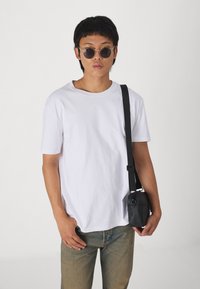 Hvit bomulls T-skjorte, korte ermer, rund hals, kombinert med lyseblå denim og en liten svart crossbody-veske. Runde solbriller fullfører antrekket.