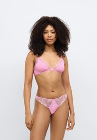 Ró�żowy komplet bielizny składający się z braletki z koronkową lamówką oraz dopasowanego stringa, podkreślający gładką fakturę i delikatne detale projektu.