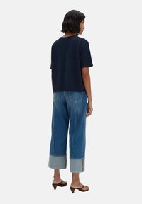 Top a maniche corte in navy a coste abbinato a jeans a gamba larga in denim chiaro, con dettagli a contrasto sui polsini e accenti di cucitura sottili.